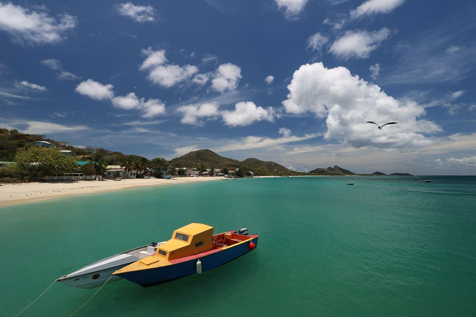 A small boat moored in clear turquoise water off a beach on Carriacou