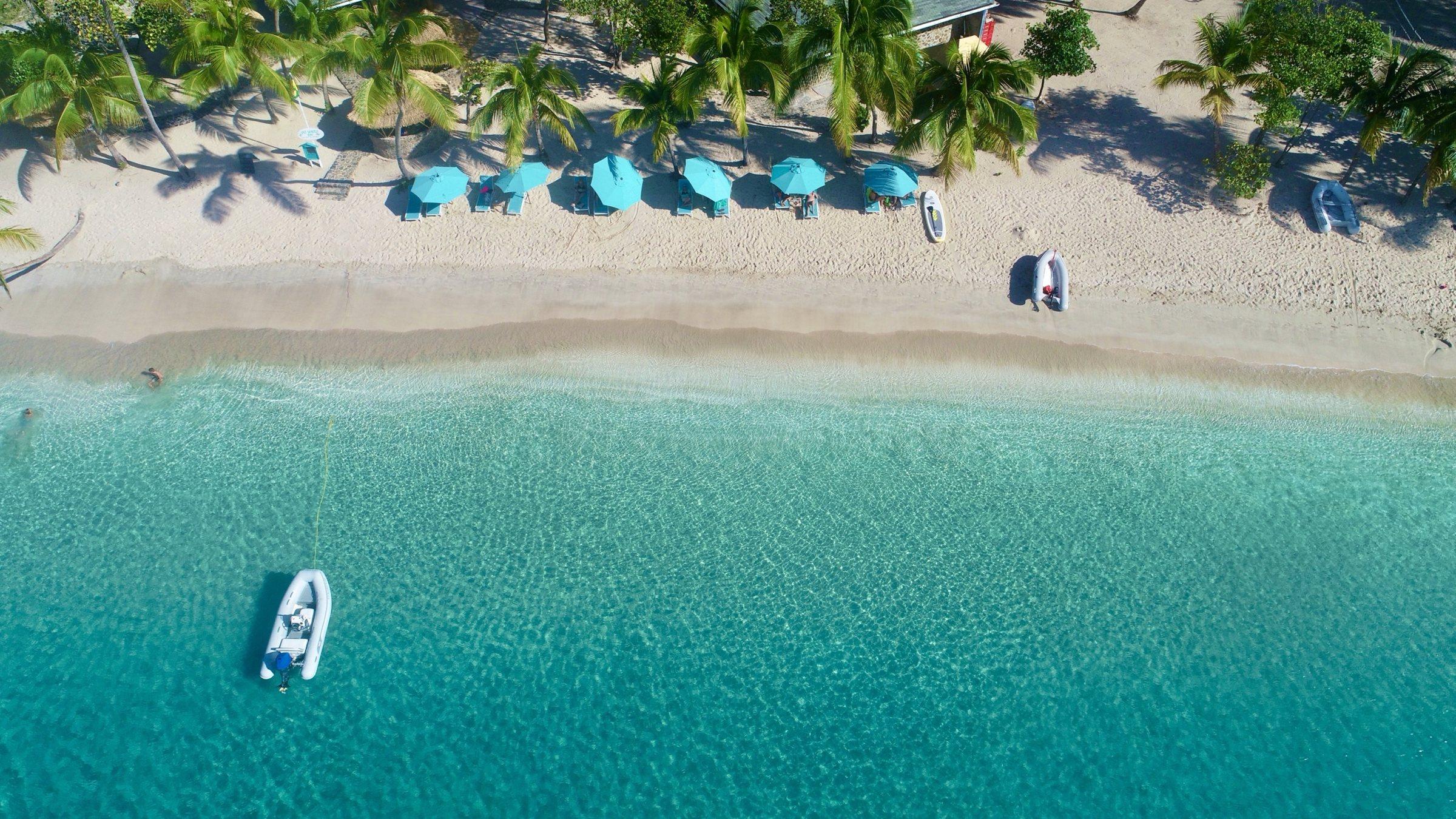 Looking down on turquoise umbrellas, palms and a white-sand beach at Salt Whistle Bay on Mayreau, with a dinghy in the clear water
